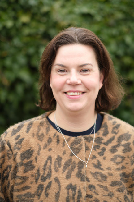 GreenRibbon_Mia_Norgren Mia Norgren ler mot kameran med en grön häck i bakgrunden. Hon har axellångt mörkt hår och bär en tröja med leopardmönster samt ett enkelt halsband. Bilden är tagen utomhus i dagsljus.